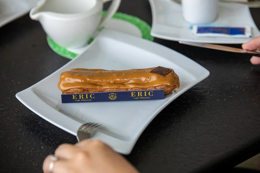 A chocolate éclair served on a By Eric plate with a coffee